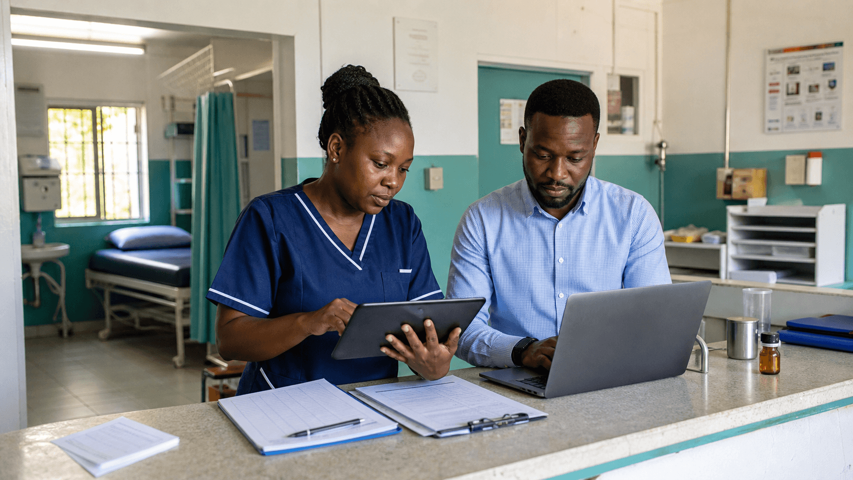 Clinic staff continue care with a tablet and laptop while paper forms sit nearby.